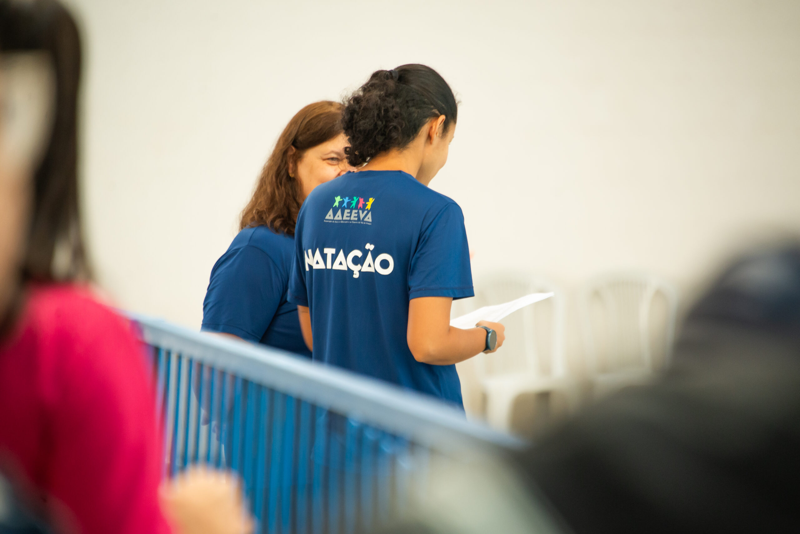 Professoras da equipe de natação da AAEEVA conversam durante um evento na piscina.