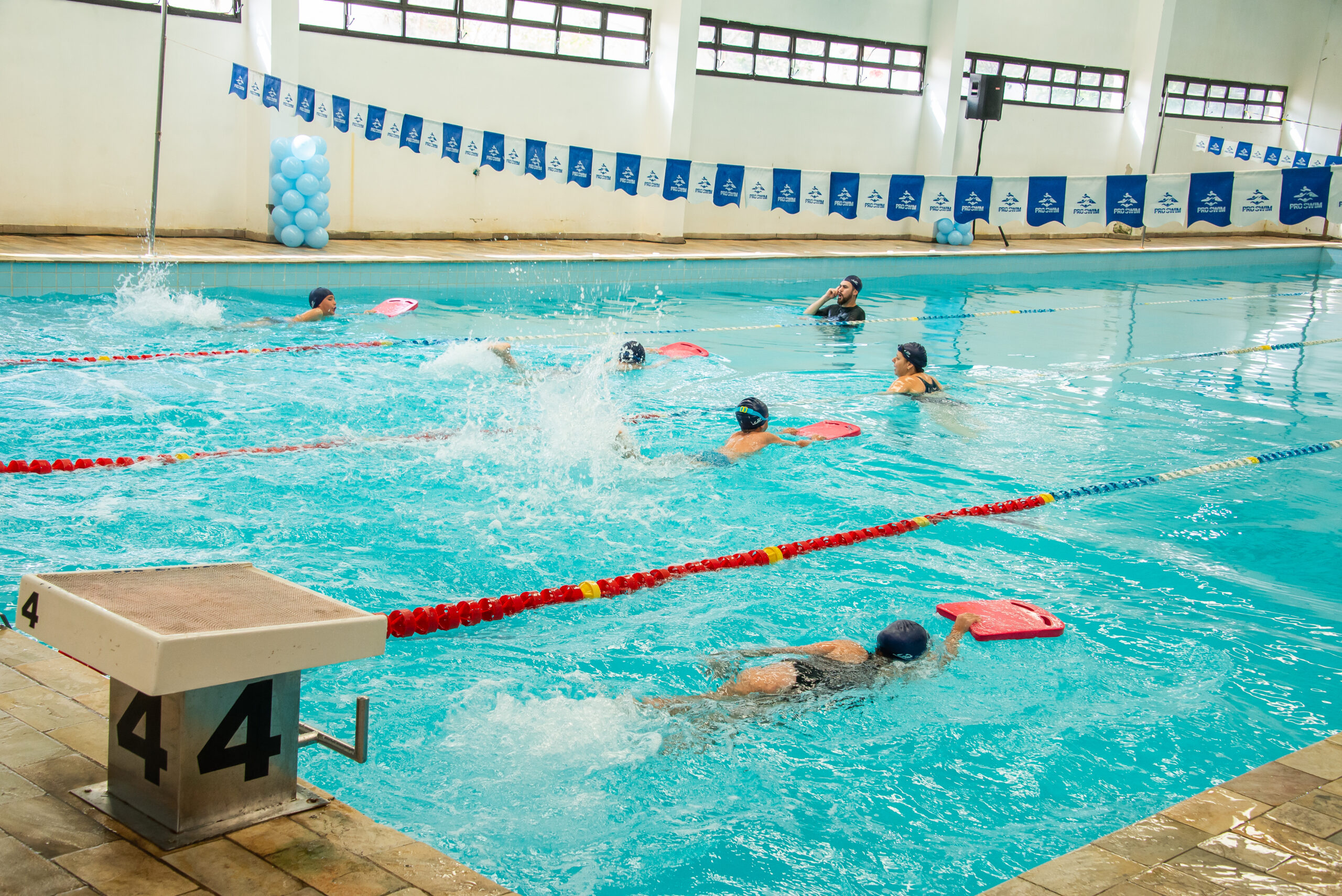 Crianças praticam natação com pranchas em uma piscina.